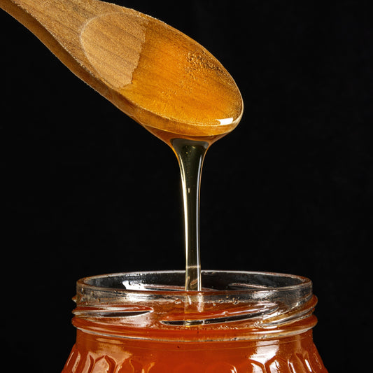 Pure raw honey dripping from wooden spoon into glass jar by Satvik Honey